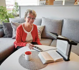 A person using the Magnilink Voice II, a text-to-speech device, to read a book while sitting on a couch.