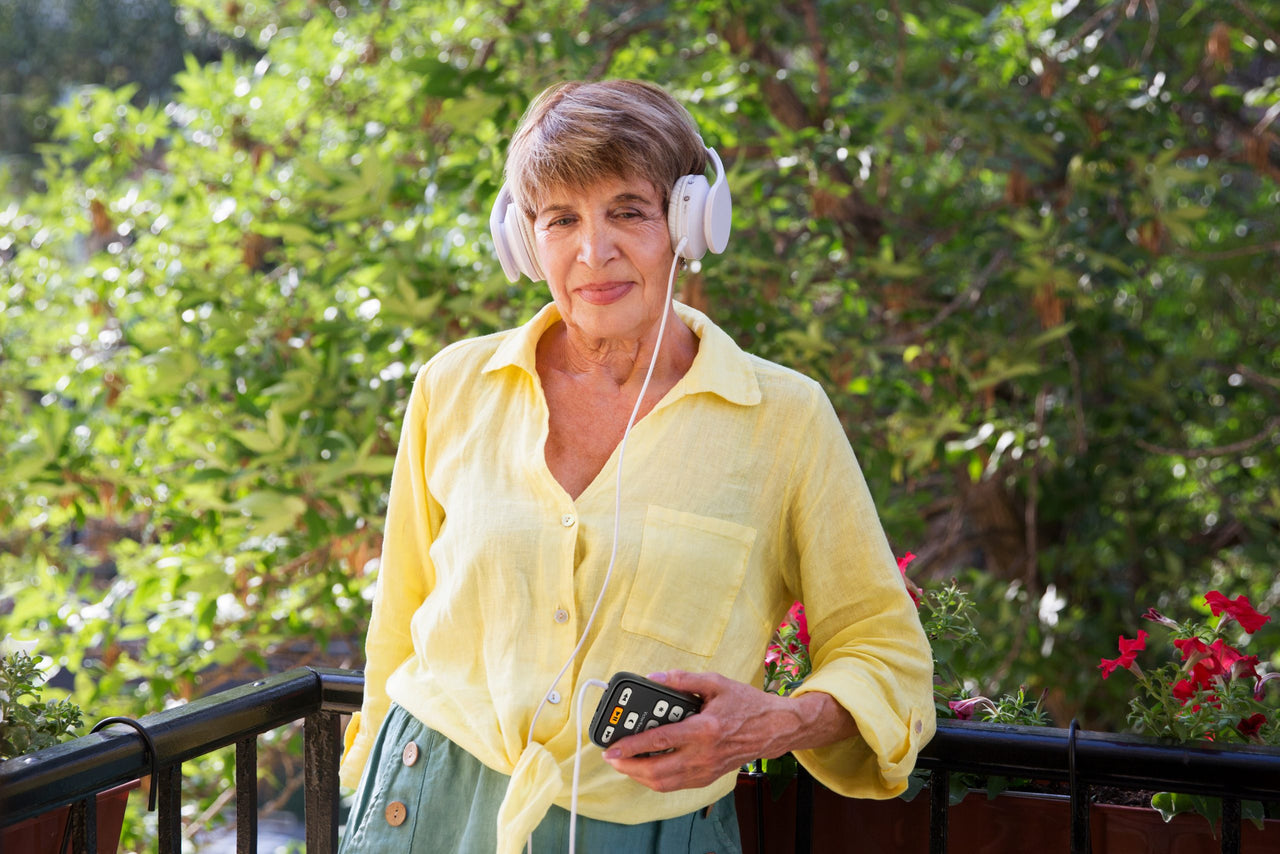 A woman with headphones on and holding a Florida Reading Victor Reader Trek.