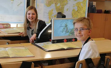 Two students using the MagniLink Zip portable video magnifier in a classroom setting, reading large-print books with ease. Available at floridareading.com