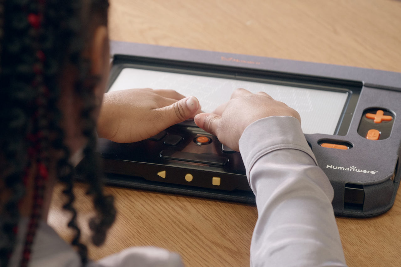 Hands(student) using a Monarch braille display, showcasing its tactile interface and control buttons.