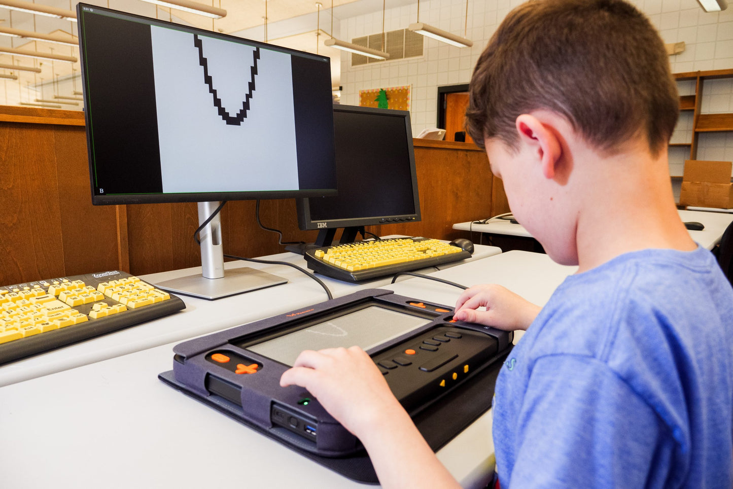 Person using a Monarch braille display connected to a computer, showcasing assistive technology for visually impaired users.