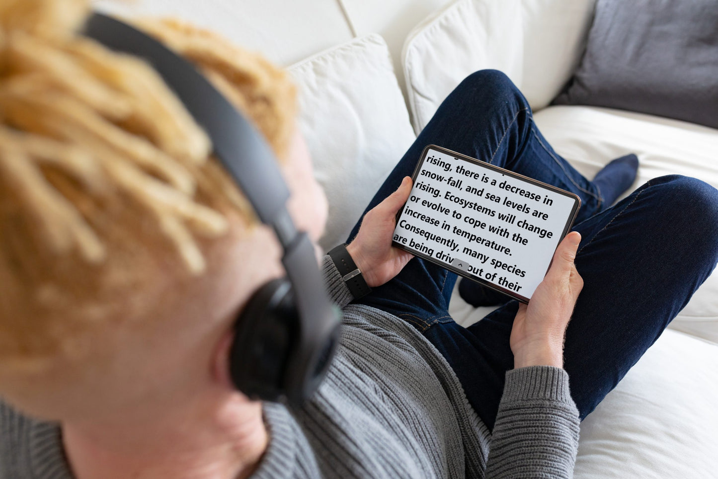 A man wearing headphones uses a tablet on a couch, demonstrating the ease of Prodigi Software in a comfortable setting.