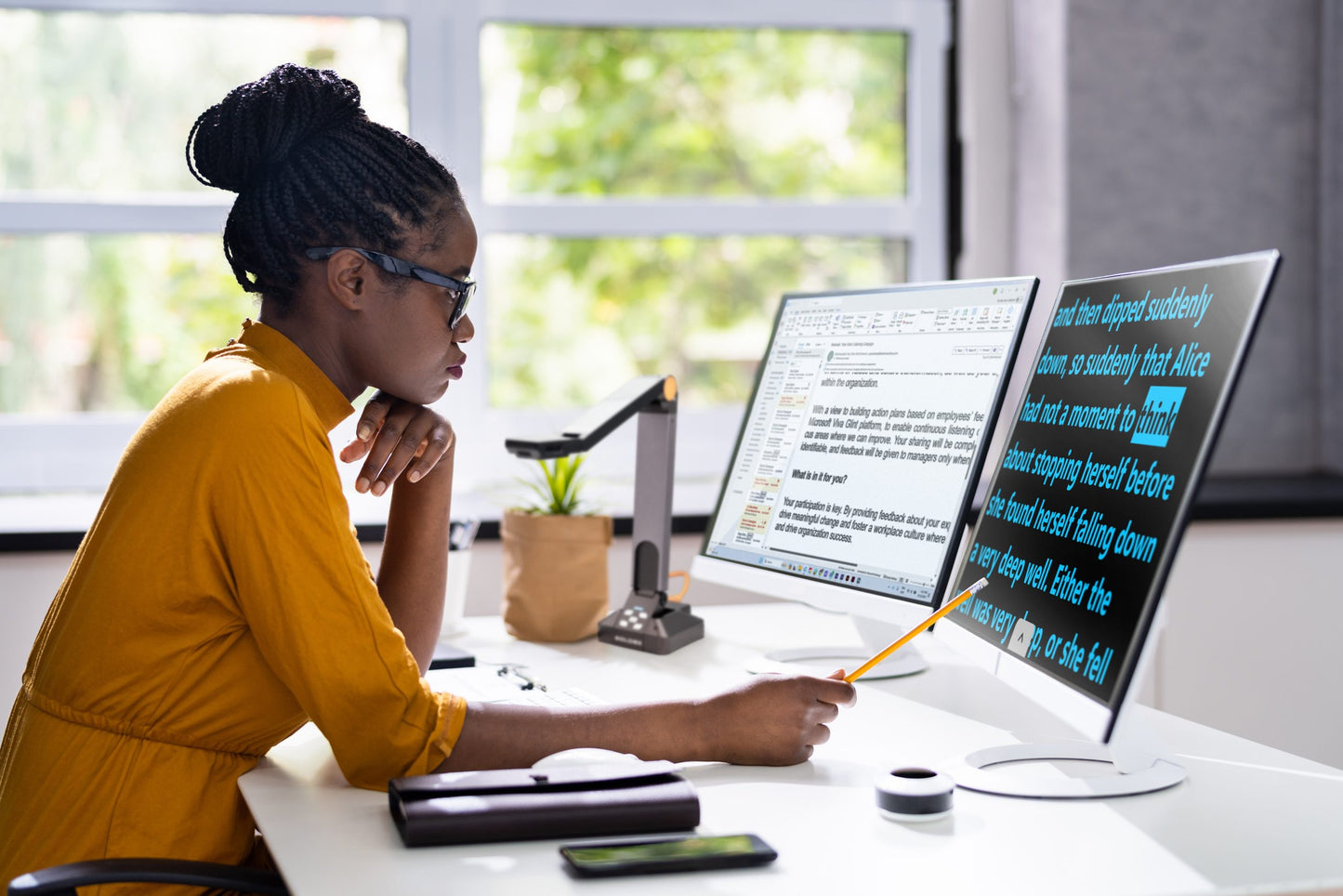 A woman using dual computer screens with Prodigi technology, focusing on magnified text on one screen in a professional workspace.