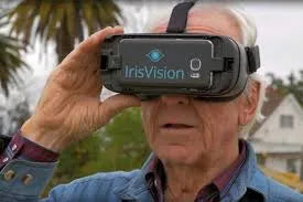 An elderly man using an IrisVision virtual reality headset outdoors, demonstrating the use of advanced assistive technology for enhancing vision.