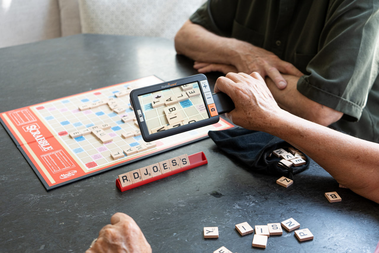 Person using Explore 5 Electronic Magnifier to read Scrabble tiles during a game.