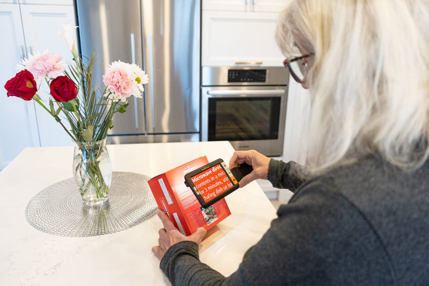 Woman using Explore 5 Electronic Magnifier to read microwave instructions on a food box.