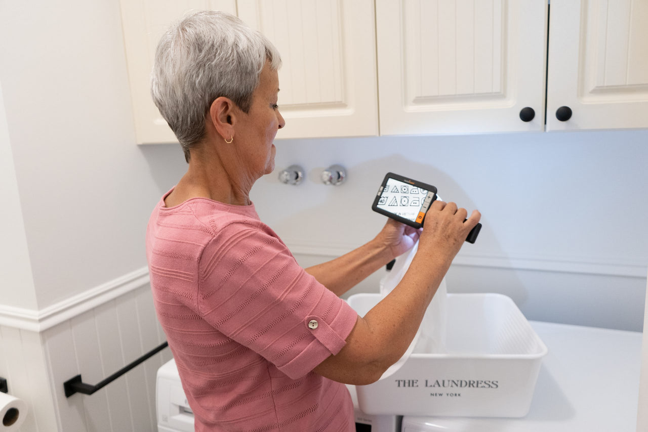 Woman using Explore 5 Electronic Magnifier to read laundry symbols