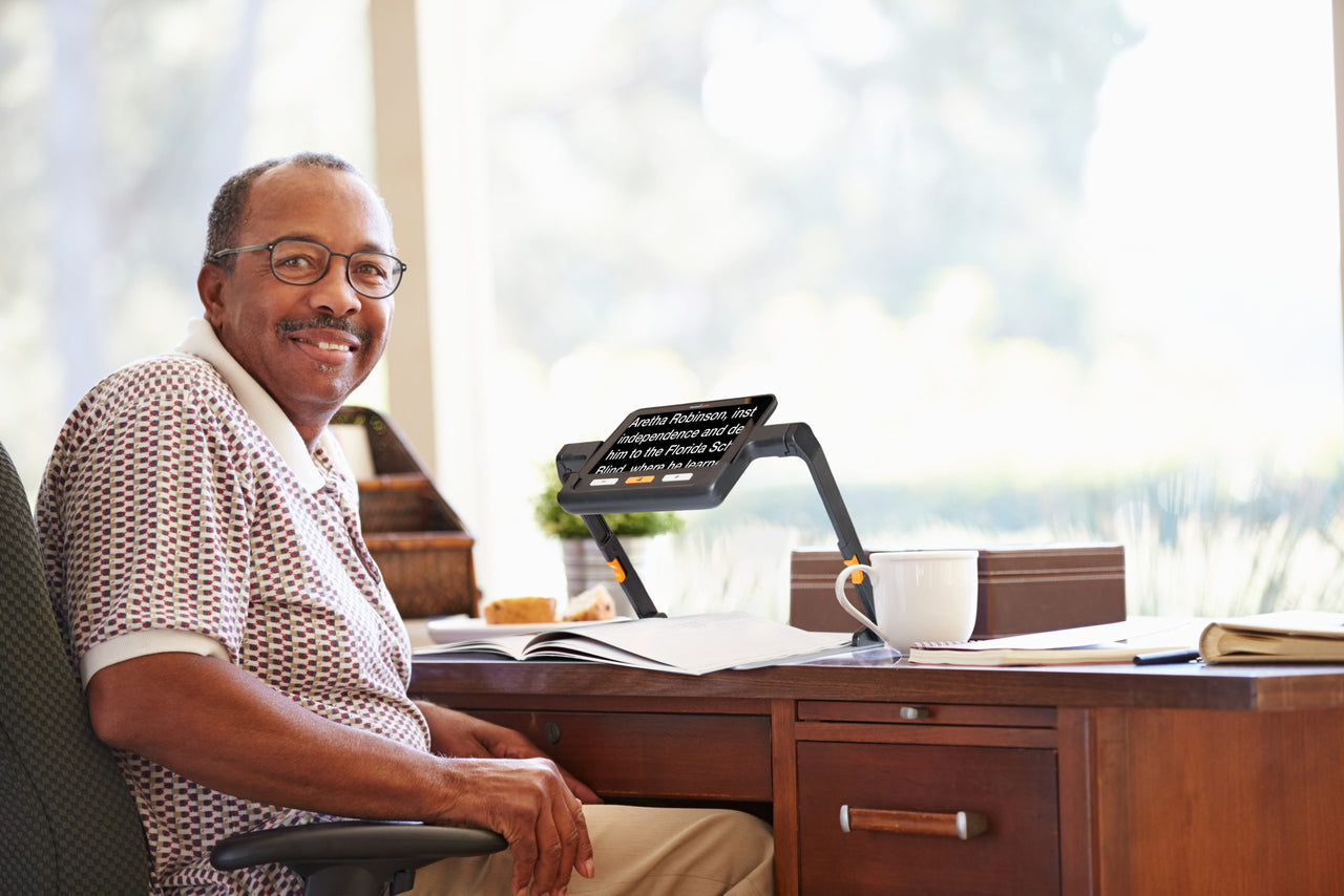 Man reading a book with a digital magnifier at his desk.