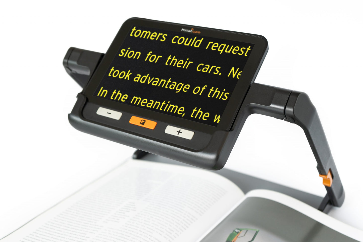 A desktop magnifier with a large screen, magnifying text from a book. The device has a Humanware logo and controls for zooming and adjusting brightness.