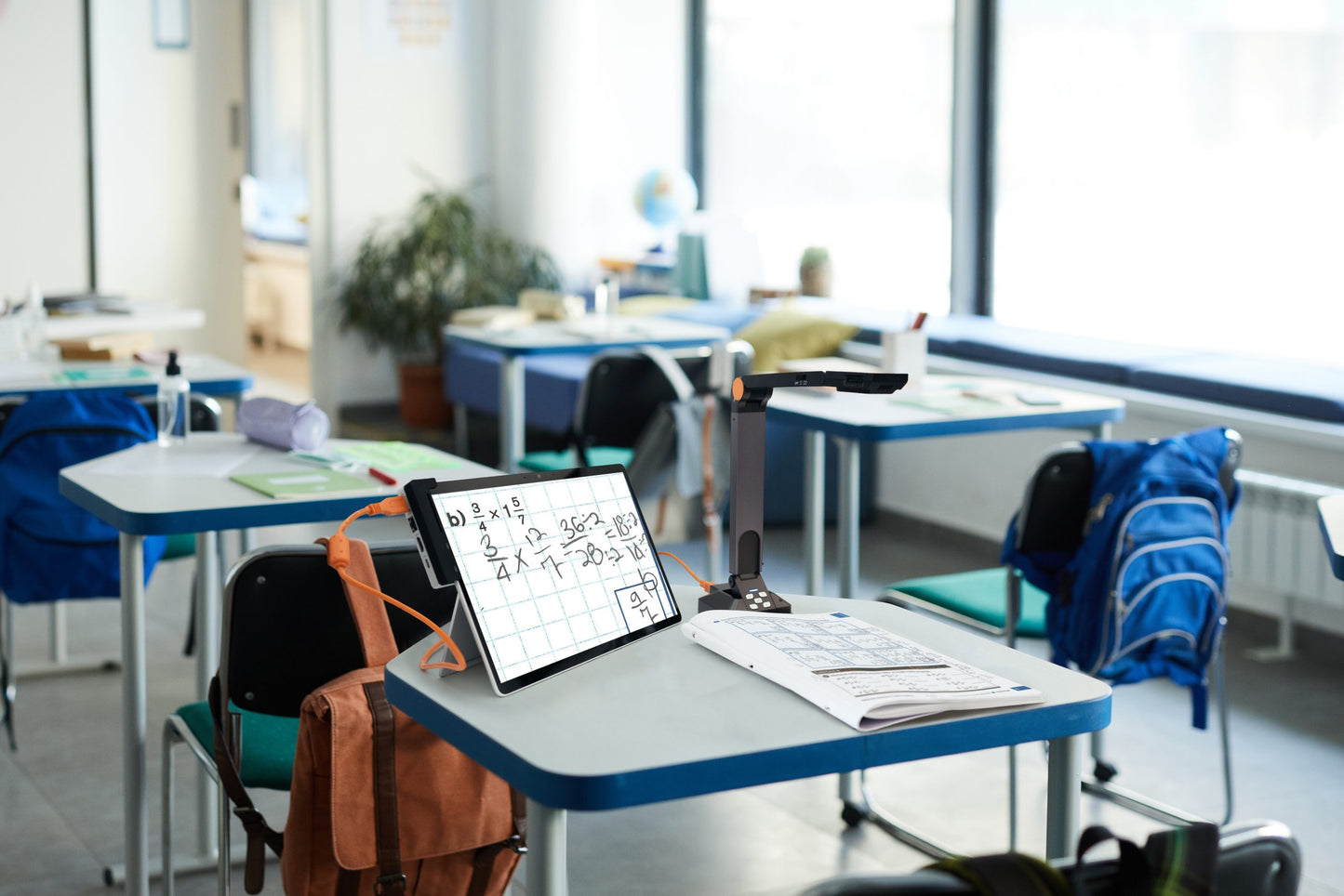 A classroom with a tablet displaying Prodigi Software Complete Kit, a projector, and backpacks on desks.